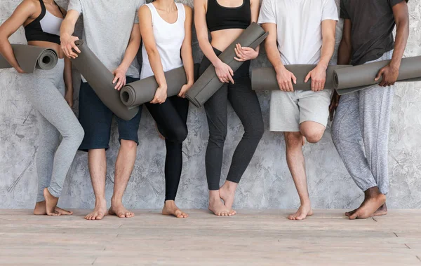 Conceito de Bem-Estar. Pessoas desportivas com tapetes de ioga em pé perto da parede cinza — Fotografia de Stock