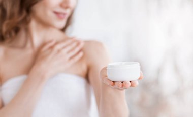 Elinde krema kavanozu olan sıska bir kadın, vücudunu besliyor.