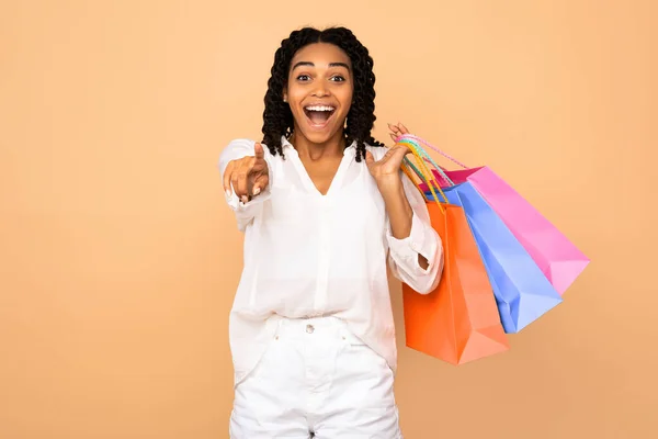 Chica Shopaholic señalando dedo posando con bolsas de compras, fondo beige —  Fotos de Stock