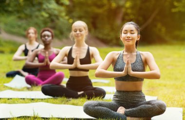 Nilüfer çiçeğinde meditasyon yapan bir grup genç kadın parkta yoga kursunda poz veriyor.