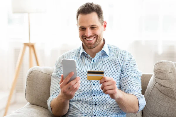 Cheerful man holding smartphone and credit card — Stock Photo, Image