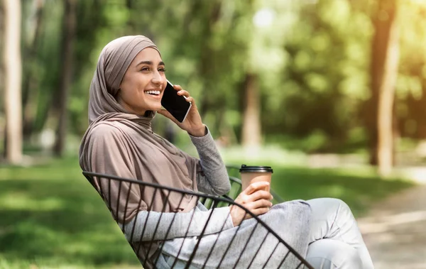 Muslim riang wanita muda beristirahat di taman, berbicara di telepon — Stok Foto