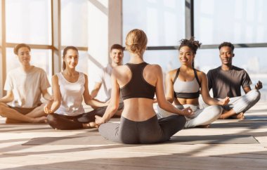 Profesyonel Yoga koçu, birlikte meditasyon yapan bir grup gençten ders alıyor.