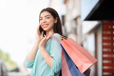 Alışveriş torbaları tutan ve cep telefonuyla konuşan Asyalı genç bir kadın.
