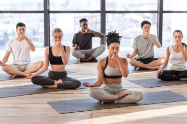 Yoga stüdyosunda genç erkekler ve kadınlar alternatif burun delikleri nefes egzersizleri yapıyorlar.