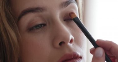 Göz farı süren, aynaya bakan genç bir kadın.