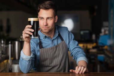 Bira ve barmen. Önlüklü yakışıklı adam bir bardak biraya bakıyor.