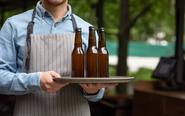 Bebidas para companhia em área aberta de pub. Garçom carrega bandeja com garrafas de cerveja — Fotografia de Stock
