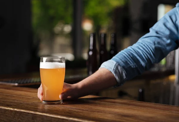 Oktoberfest no pub. Bartender mão detém cerveja lager em vidro no interior do bar — Fotografia de Stock