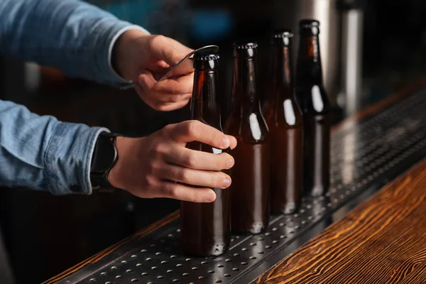 Barmen, ahşap tezgahta bira ile bir sürü cam şişe açar. — Stok fotoğraf