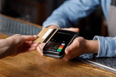 Müşteri bardaki içkilerin parasını ödüyor. Barmen terminali tutuyor, kadın eli de kredi kartını.
