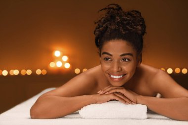 Gülümseyen siyah kadın masaj masasında yatıyor.