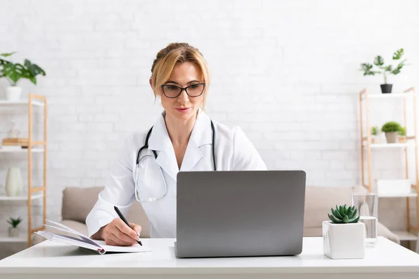 Работа из дома. Женщина врач за столом в комнате с ноутбуком — стоковое фото