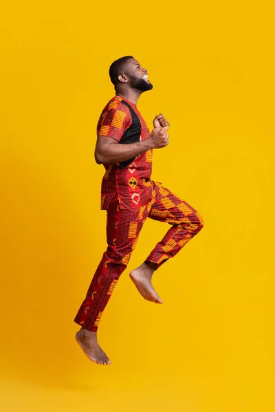 Feliz homem negro descalço em traje africano pulando no ar — Fotografia de Stock