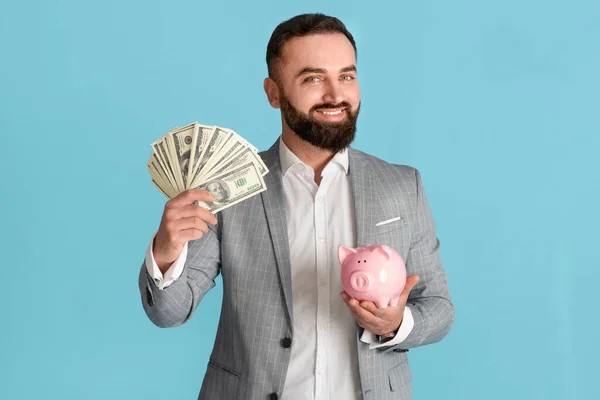 Glimlachende ondernemer met veel geld en spaarvarken op blauwe achtergrond — Stockfoto