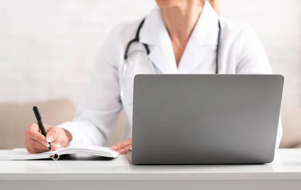 Online doctor consultation. Woman in white coat makes notes with pen and notebook