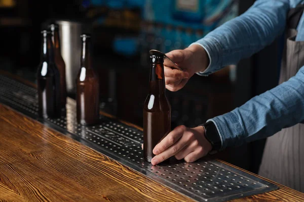 Bebida fria para clientes. Barman garrafa aberta de cerveja no bar de madeira — Fotografia de Stock