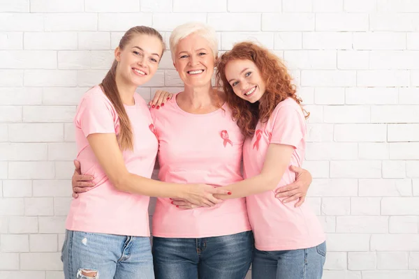 Tre signore in t-shirt con il nastro del cancro che abbraccia, sfondo bianco — Foto Stock