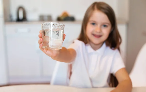 Девушка показывает стакан воды на камеру, сидя на кухне — стоковое фото