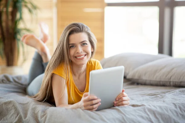 Mujer milenaria sonriente usando tableta para el trabajo en línea o la educación en la cama en casa, espacio en blanco — Foto de Stock