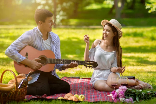 Namorado afetuoso tocando guitarra e cantando música para sua namorada durante o piquenique de verão no parque — Fotografia de Stock