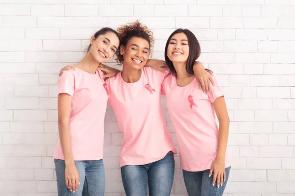 Mulheres alegres em camisetas de câncer de mama rosa abraçando perto da parede — Fotografia de Stock