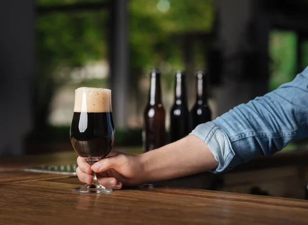 Relájate en el pub. barman mano poner en barra de madera contador de un vaso de cerveza oscura con espuma — Foto de Stock