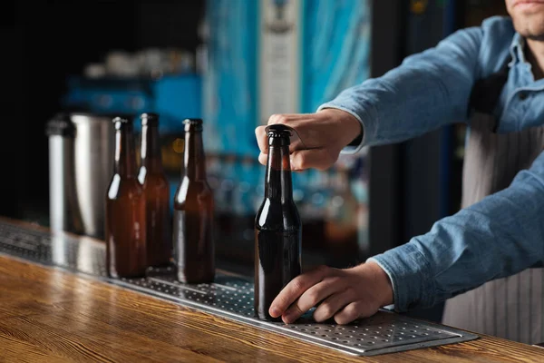 Leisure, friends company and pub. Bartender opens bottle of beer