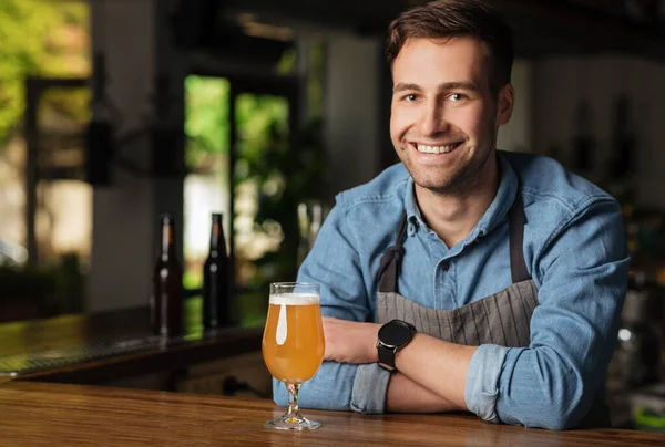 Lager fresco con espuma. Cantinero sonriente con brazos cruzados, detrás del mostrador de la barra con vidrio — Foto de Stock