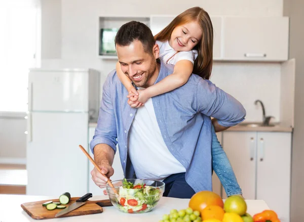 キッチンで肩の上に小さな娘を保持する幸せなお父さん料理 — ストック写真