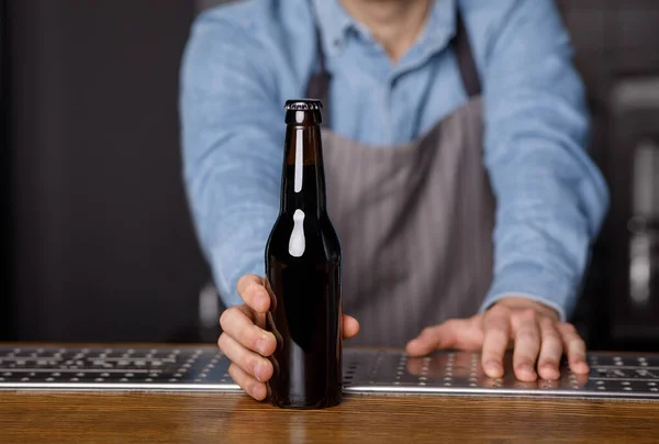 Buenas noches en el pub. Cantinero da a cliente botella de cerveza en el bar — Foto de Stock