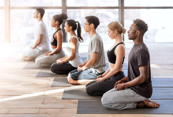 Concepto de bienestar. Jóvenes deportistas en clase de yoga haciendo ejercicios de meditación juntos — Foto de Stock