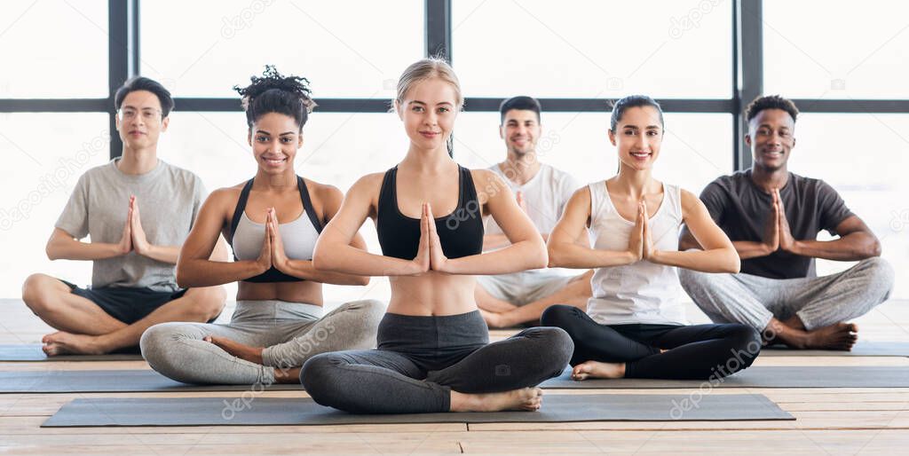 Young multiethnic yoga practitioners doing namaste gesture while meditating together in studio