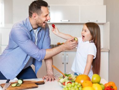 Father And Daughter Feeding Each Other Cooking Together In Kitchen clipart