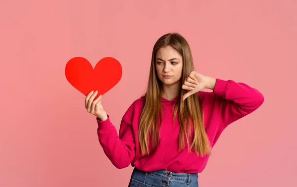 Adolescente menina segurando o coração e mostrando antipatia — Fotografia de Stock