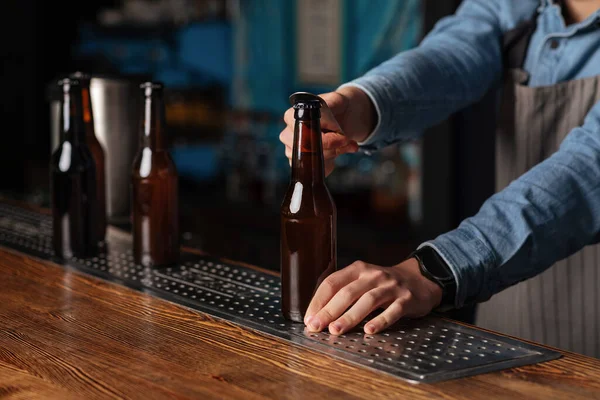 Werken in een pub. Barman opent fles bier op houten bar teller — Stockfoto