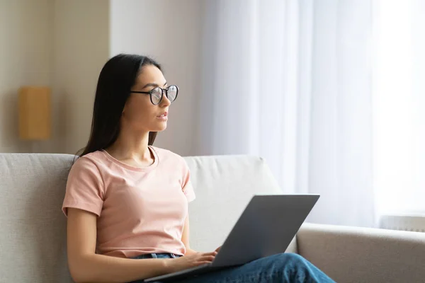 Mulher trabalhando no laptop pensando sentado no sofá em casa — Fotografia de Stock