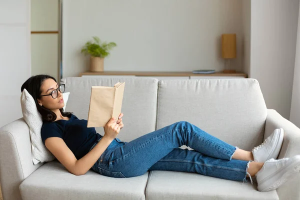 Studente ragazza lettura libro studiare sdraiato su divano a casa — Foto Stock