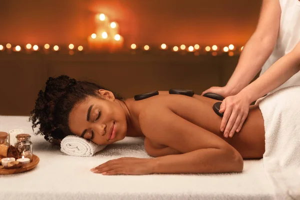 Femmina terapeuta fare pietre calde massaggio per la donna africana — Foto Stock
