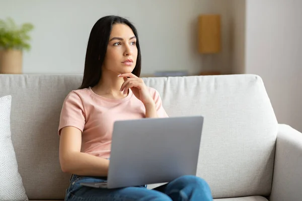Mulher Freelancer pensativa no laptop Pensando sentado no sofá dentro de casa — Fotografia de Stock