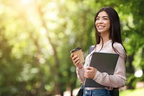 Retrato de mujer asiática sonriente caminando en parque con portátil y café —  Fotos de Stock