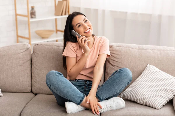 Mujer sonriente hablando en el teléfono móvil sentado en el sofá — Foto de Stock