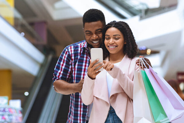 Приложение для покупок. Smiling Couple Using Cellphone Searching Sales and Discount Offers Standing In Mall Center. Пустое пространство
