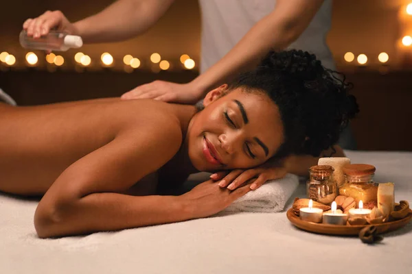 Therapeutin wendet Massageöl auf schönen schwarzen Frauenkörper an — Stockfoto