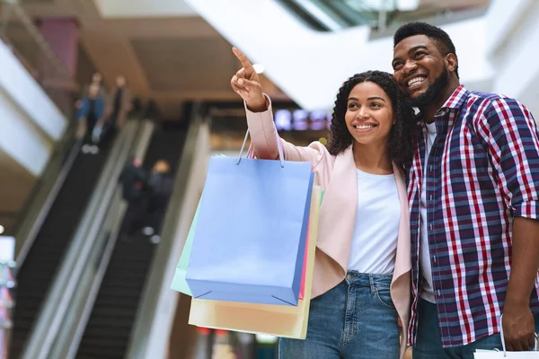 Negro millennial pareja compras juntos en centro comercial, joven mujer señalando en escaparate —  Fotos de Stock