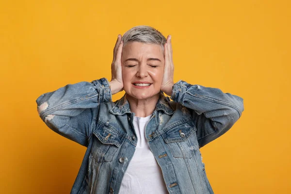 Geïrriteerde vrouw van middelbare leeftijd bedekt oortjes in stress, staande over gele achtergrond — Stockfoto