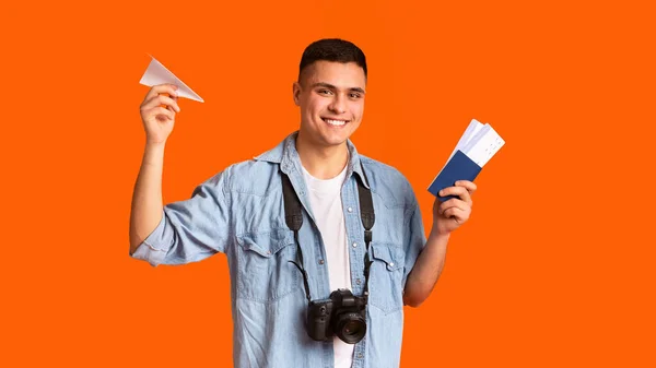 Happy traveler with camera holding passport and paper airplane