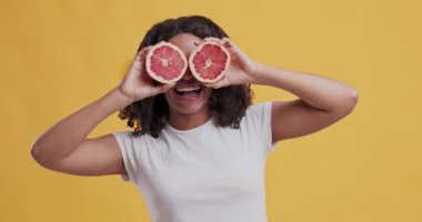 Gözlerinin yanında greyfurt tutan neşeli Afrikalı Amerikalı kadın.