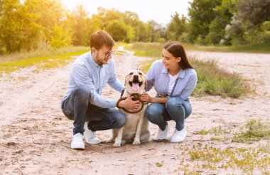 Mutlu genç bir çiftin şirin köpeklerine sarılırken portresi.