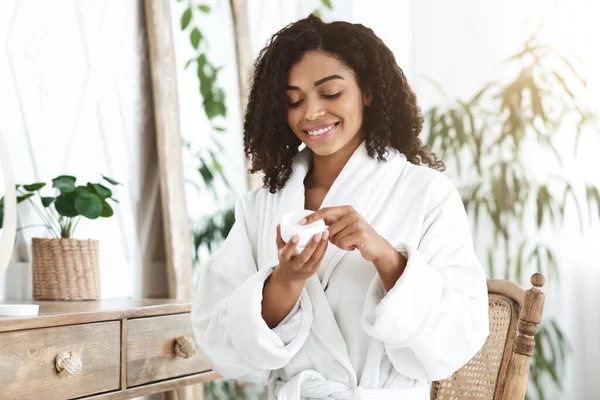 Crema para el cuidado de la piel. Sonriente mujer afroamericana sosteniendo tarro con loción hidratante —  Fotos de Stock